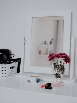 Chic vanity setup with a mirror, fresh flowers, and red lipstick on a white surface.