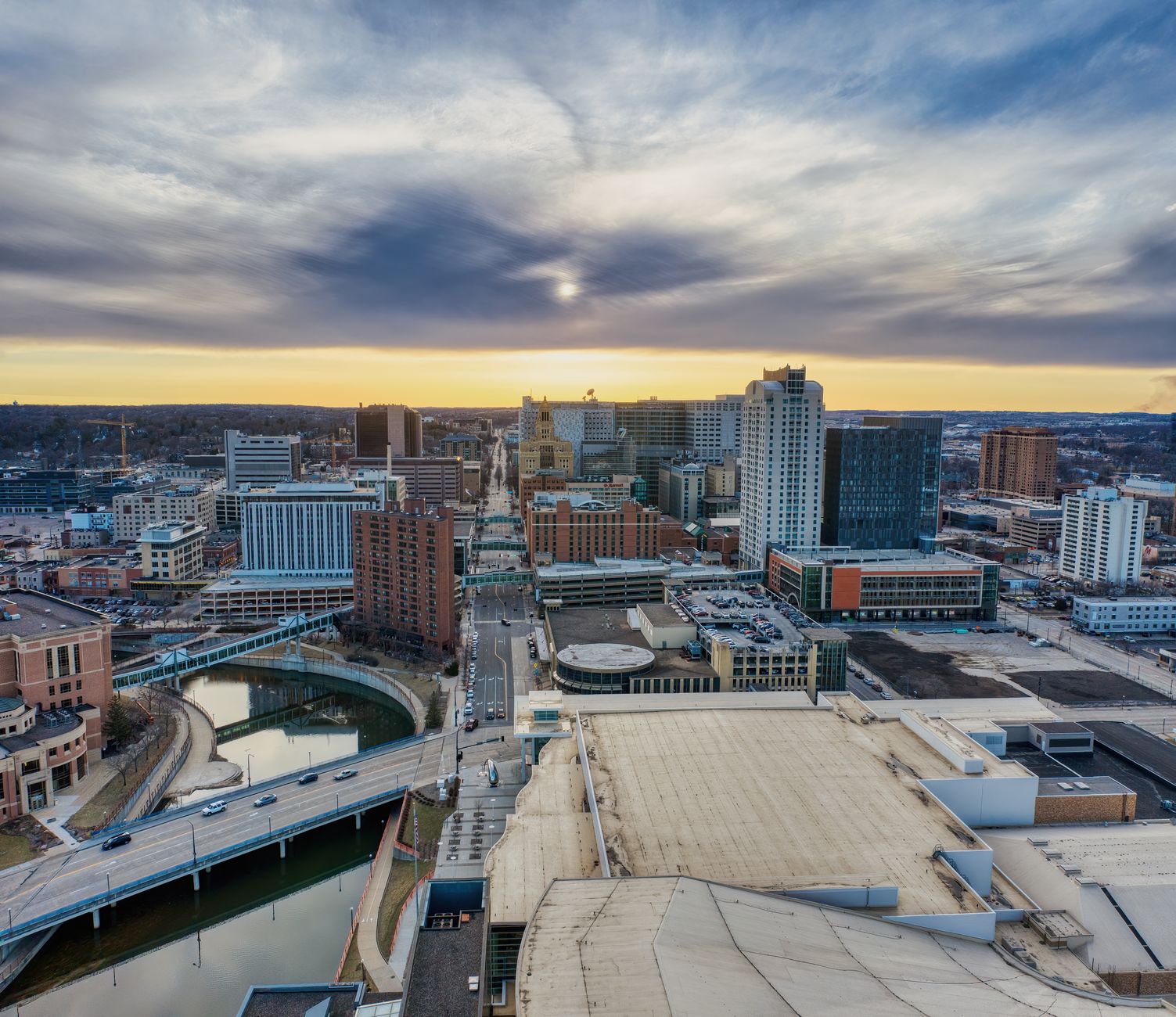 Aerial shot of Rochester, MN skyline and river at twilight under a cloudy sky.