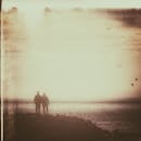 一张浪漫的复古照片，一对情侣在日落时分在海边散步，营造出一种宁静而怀旧的氛围