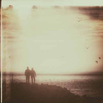 A romantic vintage photo of a couple walking at sunset by the ocean, creating a serene and nostalgic mood.