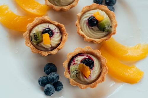 Free A close-up of assorted fruit tartlets featuring blueberries, kiwi, and peach on a white plate. Stock Photo