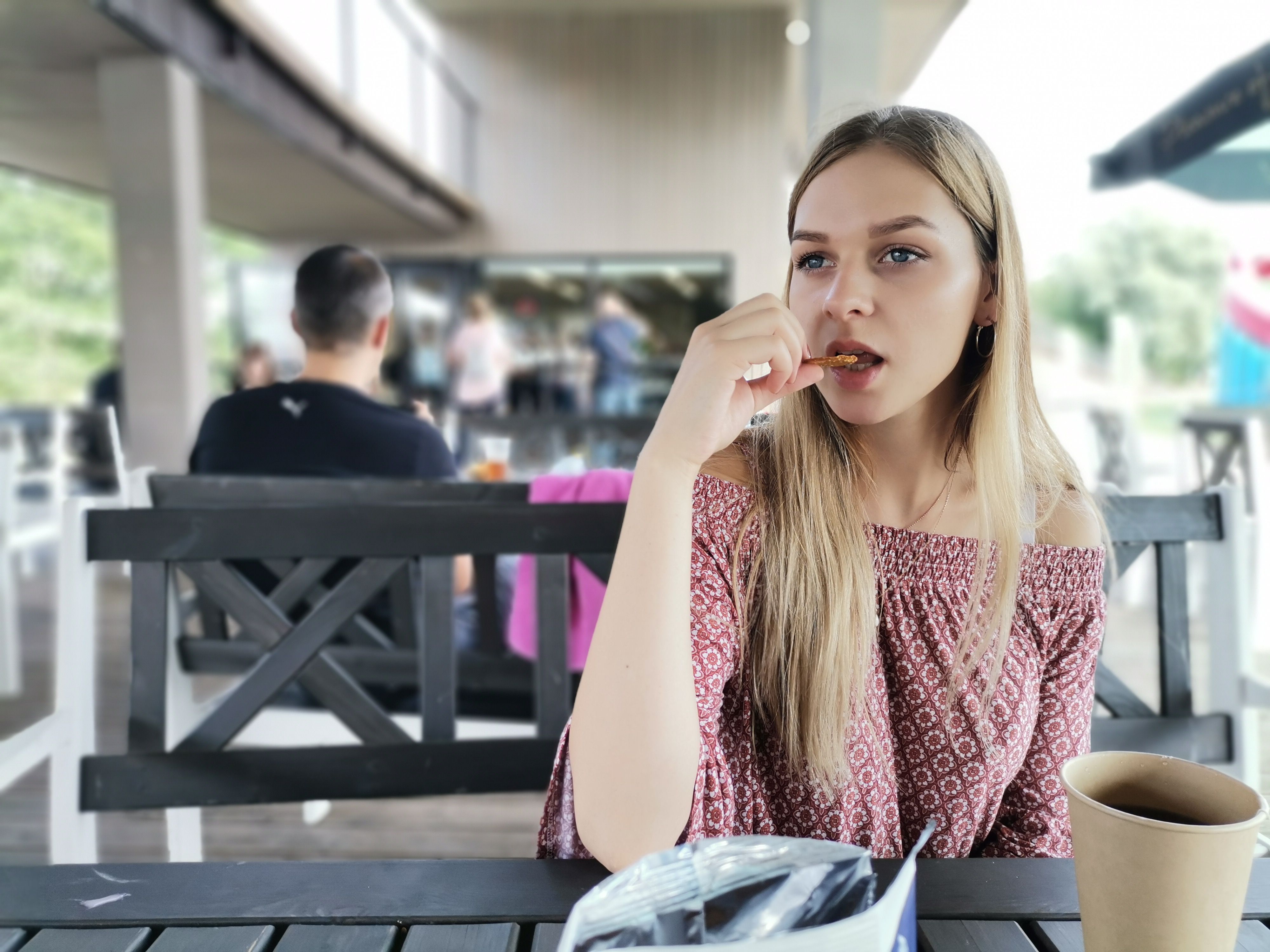 Blonde woman in a patterned top enjoying a snack at an outdoor café in Lithuania.