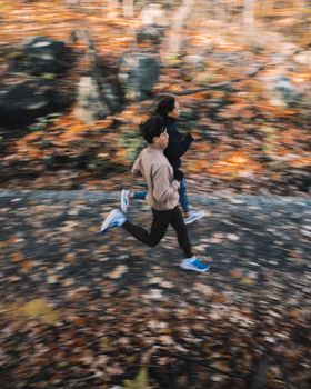 Dynamic shot of a couple running through a leafy park in Montreal during autumn, capturing motion and energy.