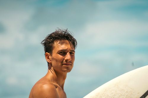 Free Close-up of a pensive young man on a sunny day at Puntarenas beach holding a surfboard. Stock Photo