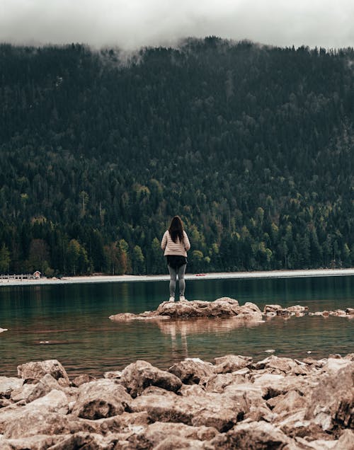 Free Woman Standing on Rocks at a Lake Stock Photo