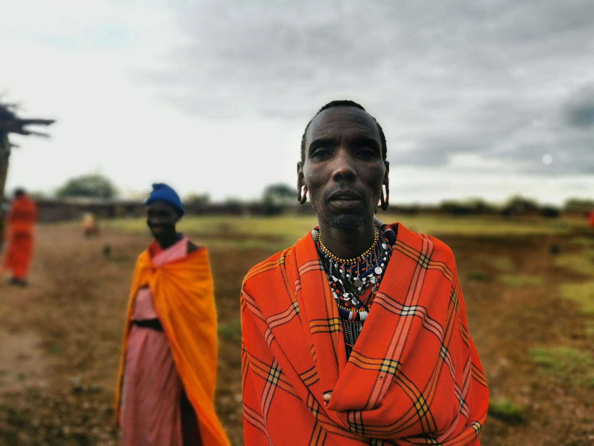 Close-up portrait of a Maasai man in traditional attire in rural Kenya with cloudy sky.