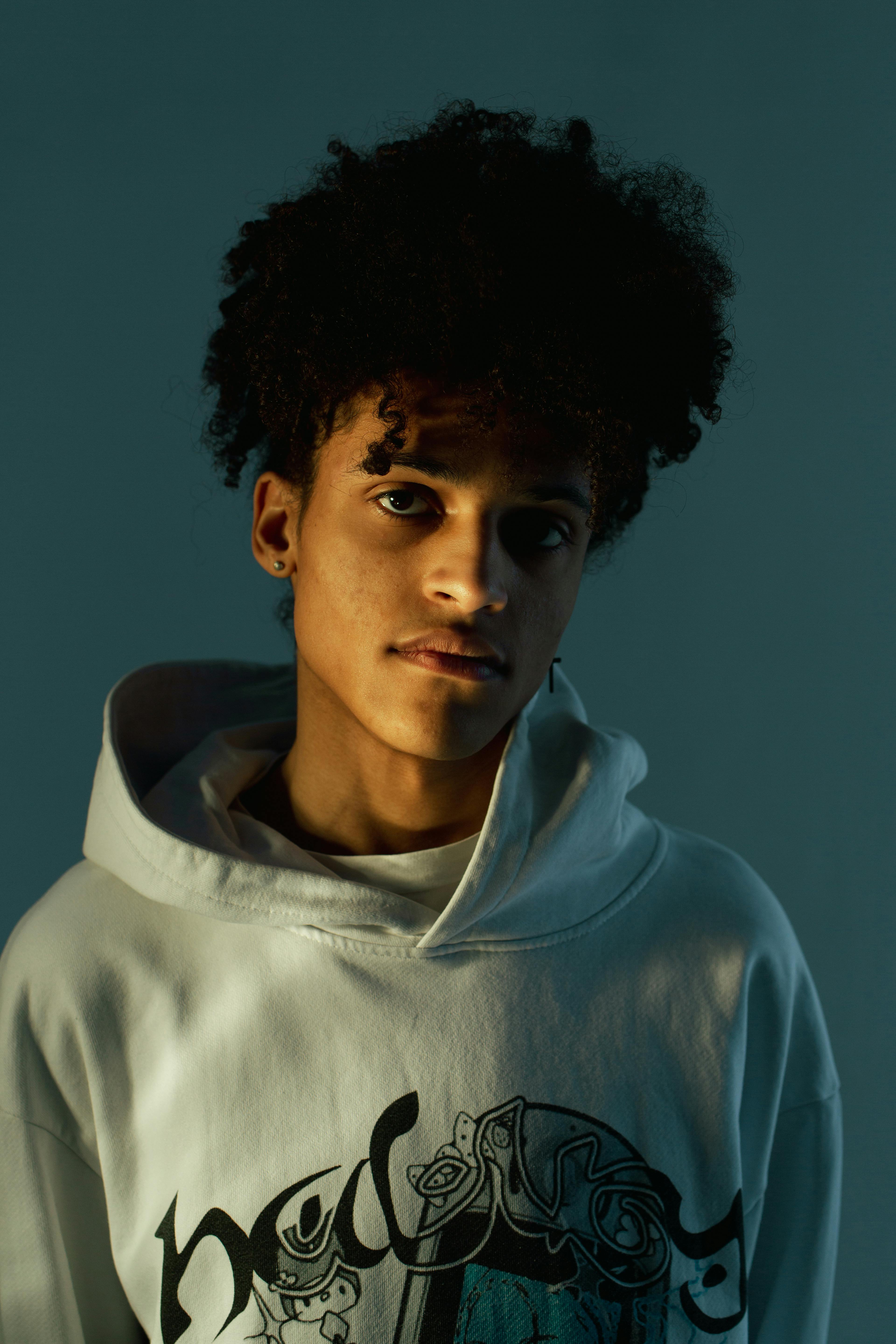Stylish portrait of a young man in a hoodie with afro hairstyle against a blue background.