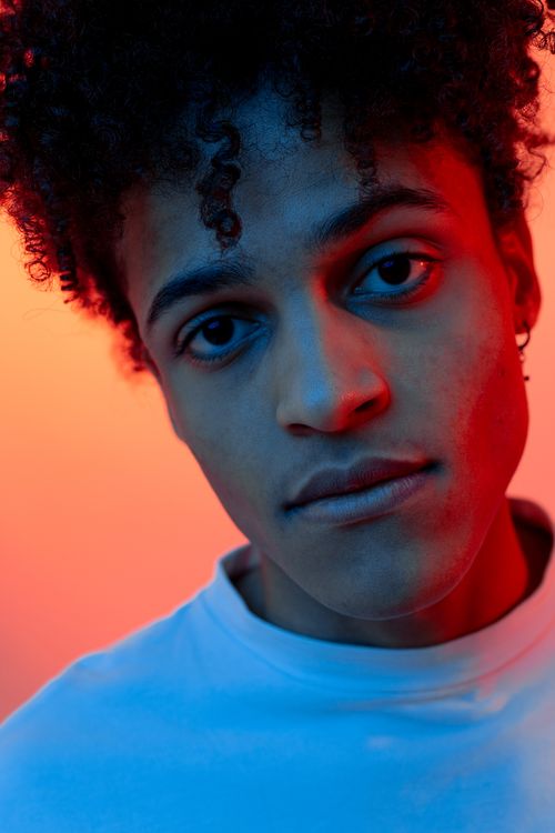 Free Dramatic close-up portrait of a young man with curly hair, captured with an artistic colorful background. Stock Photo