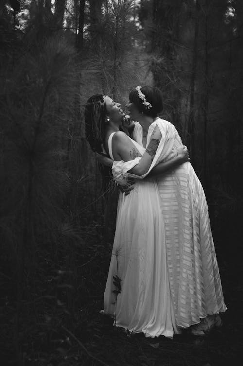 Free Two Women in Wedding Dresses Laughing and Embracing Stock Photo