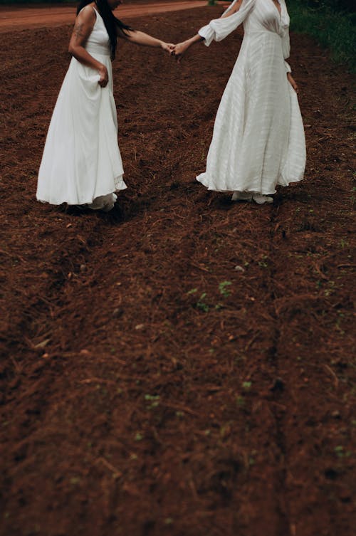 Two Women in Wedding Dresses Walking in Field 