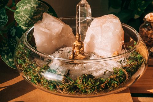 Free A serene composition featuring a Buddha statue surrounded by crystals and greenery in a glass bowl. Stock Photo