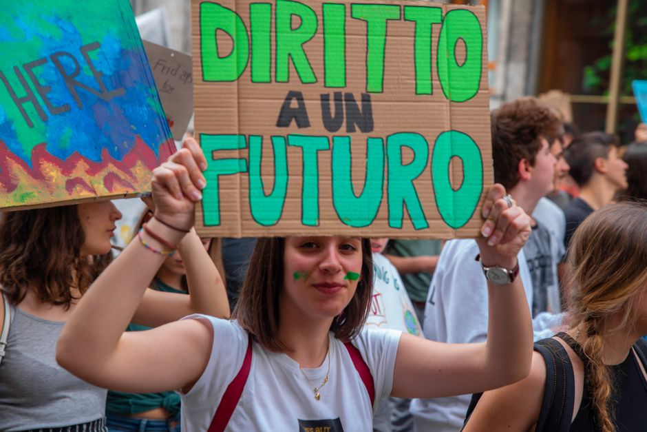 Jóvenes adultos en Milán se manifiestan por la acción climática, sosteniendo carteles en una protesta dinámica.