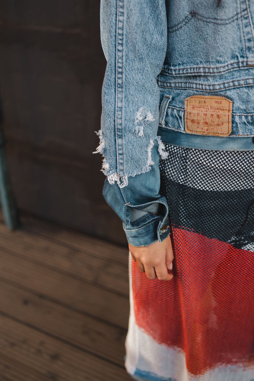 Close-up of a woman wearing a distressed denim jacket and colorful dress, showcasing trendy fashion.