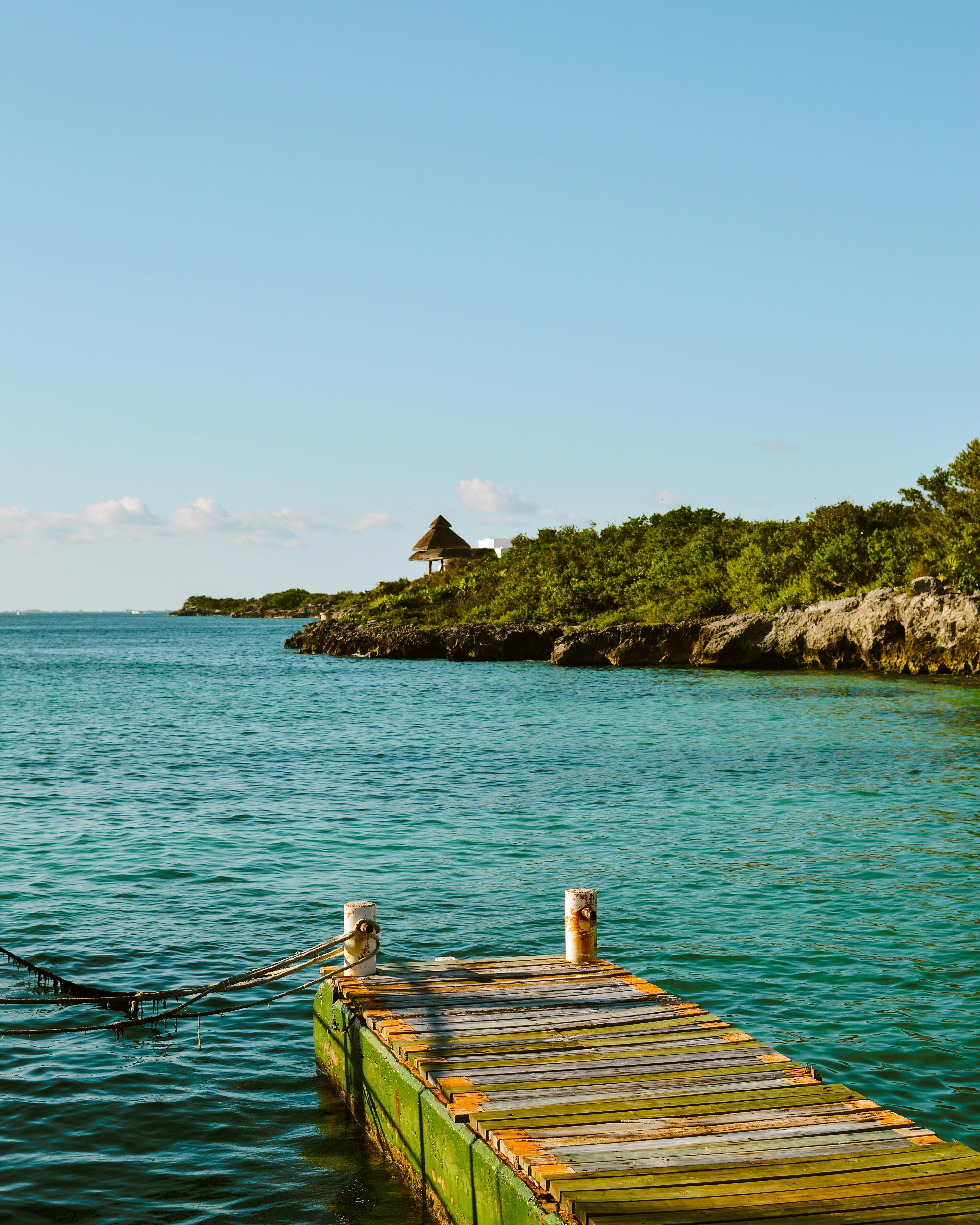 Vibrant teal waters and a wooden dock with lush greenery on Isla Mujeres, Mexico.