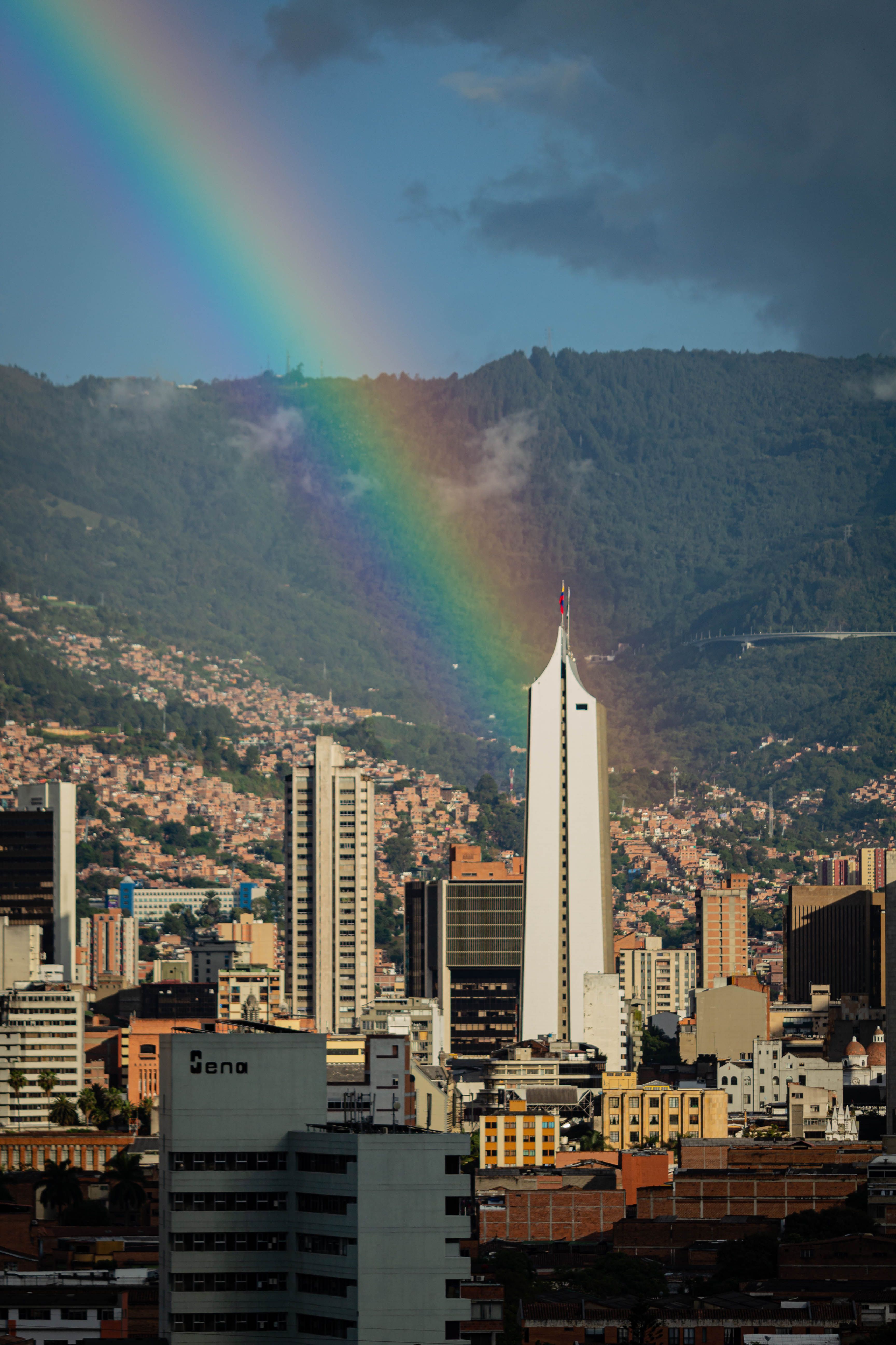 Stunning cityscape with a vibrant rainbow over mountains, showcasing urban architecture against nature.