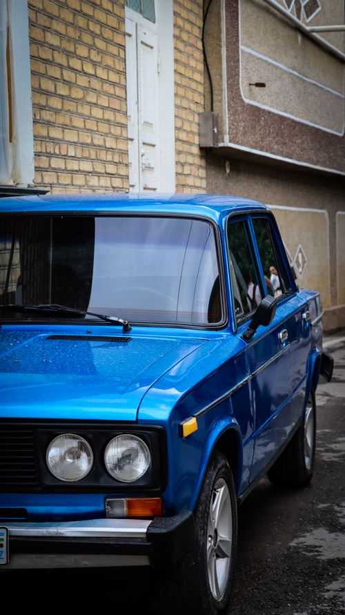 Free Close-up of a vintage blue car parked in a narrow urban alley, capturing its classic design. Stock Photo