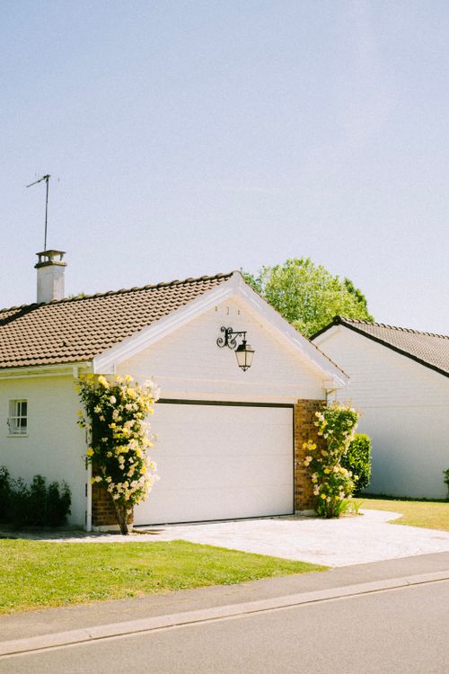Free Beautiful suburban house with a garage surrounded by flowering plants in a sunny neighborhood. Stock Photo