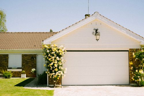 Free A lovely suburban home with a prominent garage and flowering plants, epitomizing suburban charm and tranquility. Stock Photo