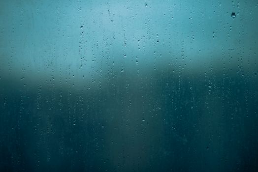 Moody image of raindrops on a window glass, capturing the essence of a rainy day.