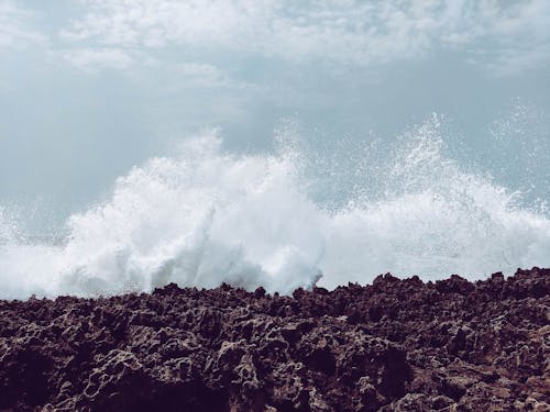 Picturesque view of white foamy waves splattering near ocean shore with rough surface under cloudy sky in daylight in stormy weather