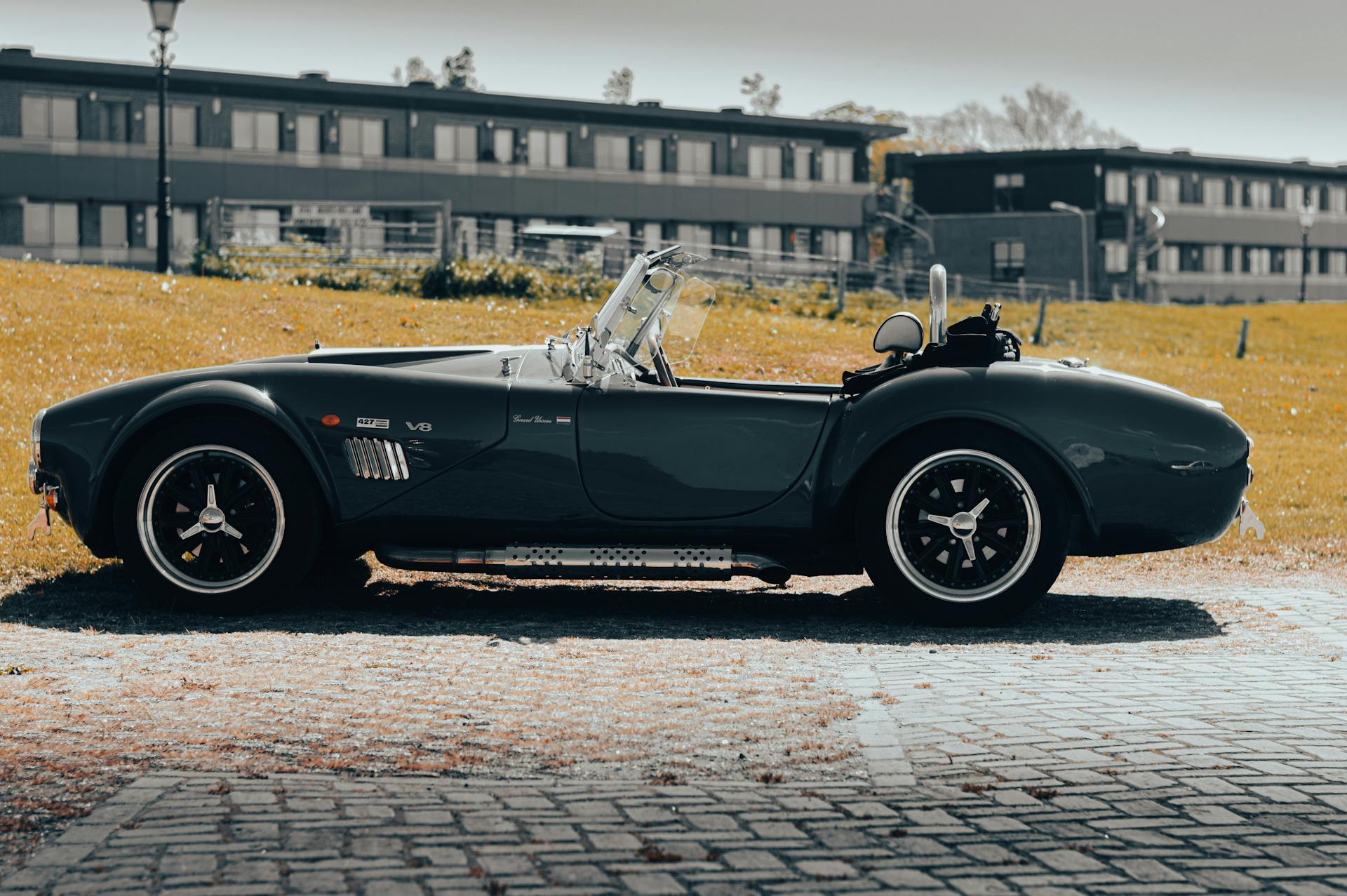 A side view of a vintage AC Cobra convertible parked outdoors on a sunny day.