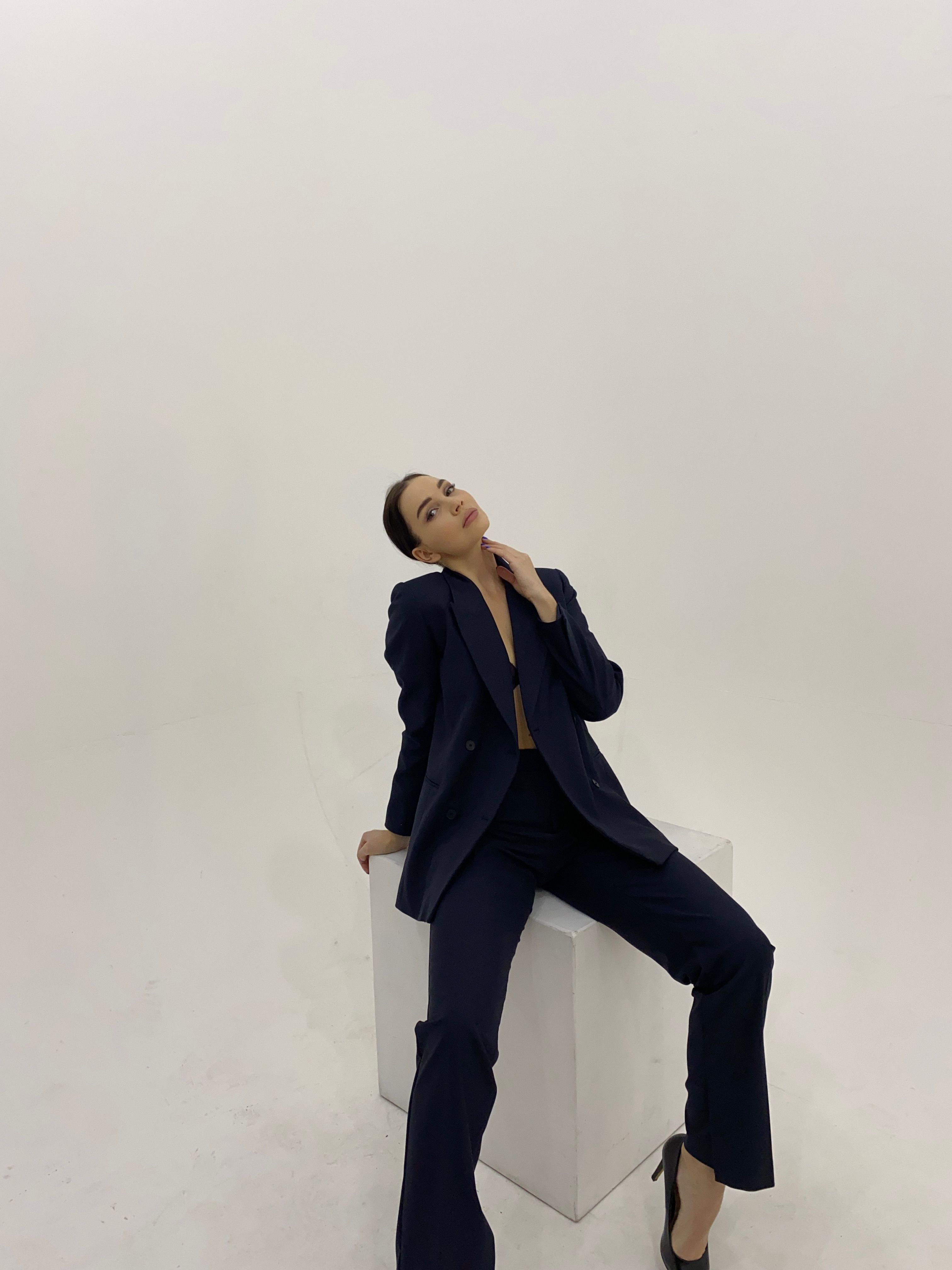 A sophisticated woman in a navy suit poses confidently in a minimalist studio setting.