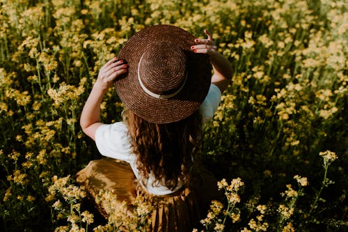 Woman Sitting on Flower Field Holding Her Hat