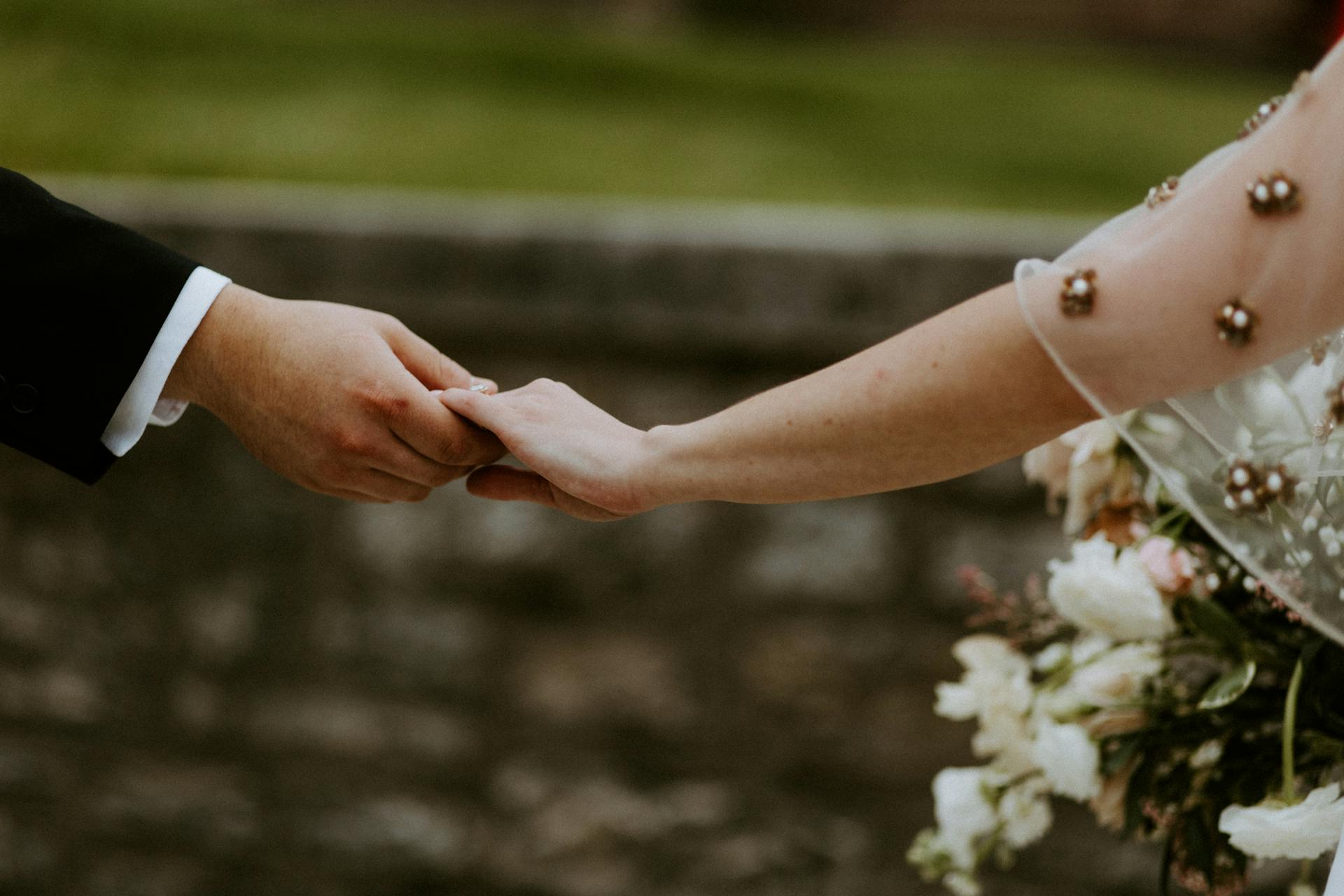 Close-up shot of a couple holding hands, symbolizing love and unity on their wedding day.