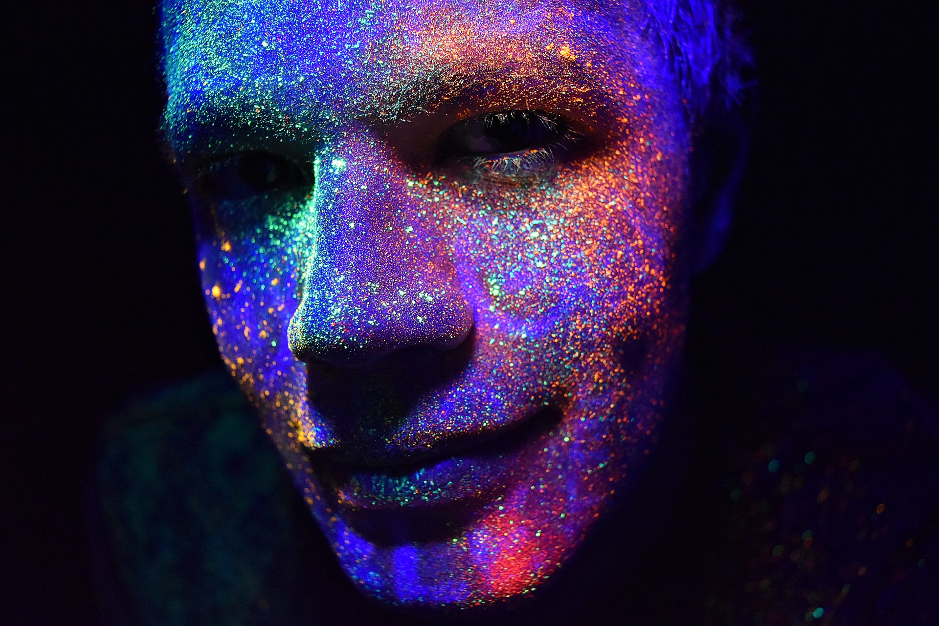 Close-up of a man's colorful face painted with fluorescent UV paint, glowing in the dark.