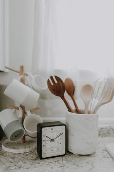 A minimalist kitchen scene featuring utensils, mugs, and a clock on the counter.