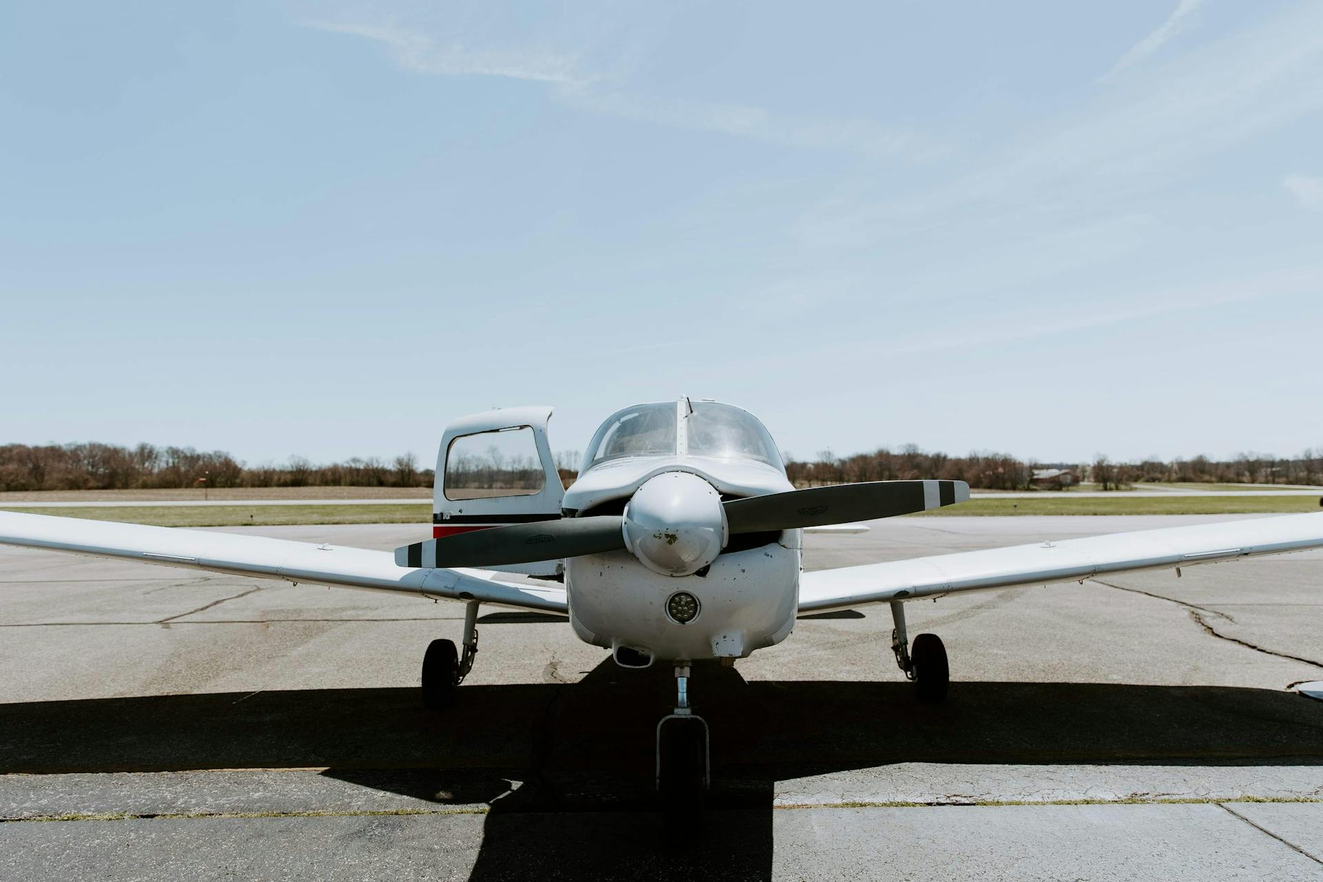 Front view of a small private aircraft parked on an airport tarmac under a clear blue sky.