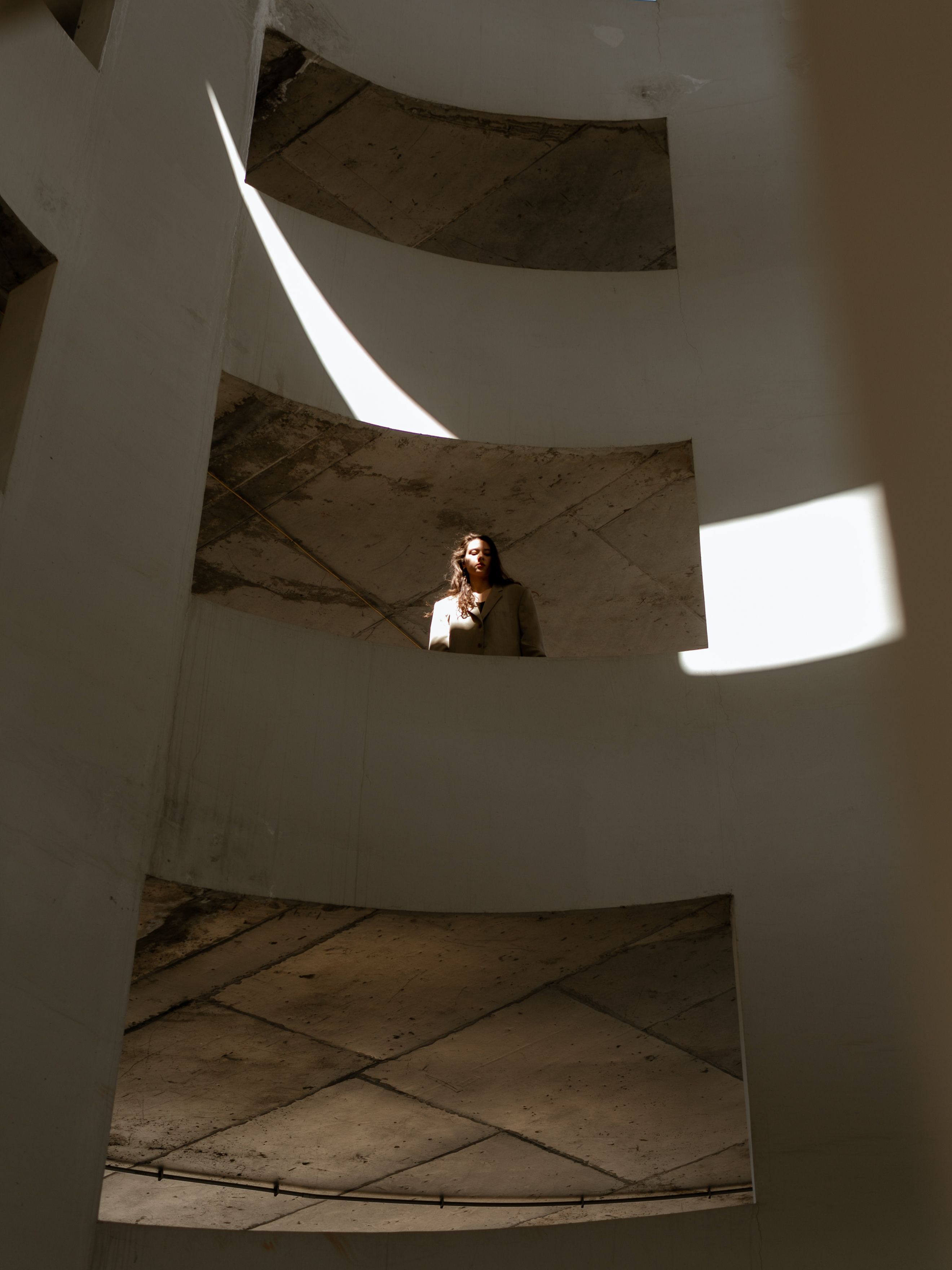 A woman gazes down from a curved structure, highlighted by dramatic sunlight.