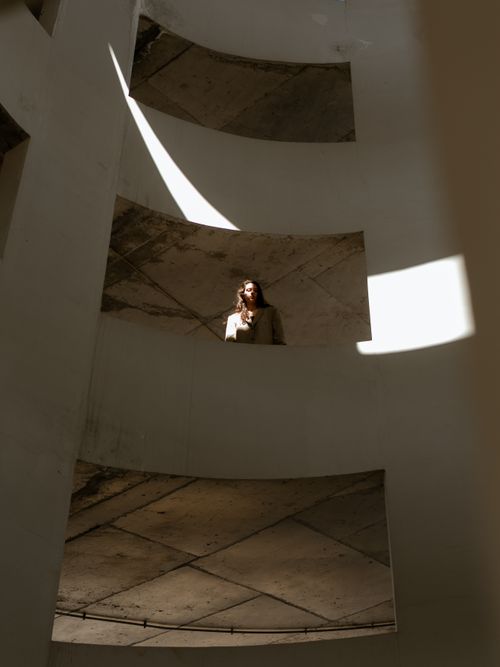Free A woman gazes down from a curved structure, highlighted by dramatic sunlight. Stock Photo