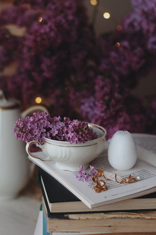 Free Purple Flowers in a Cup Near a Candle on an Open Book Stock Photo