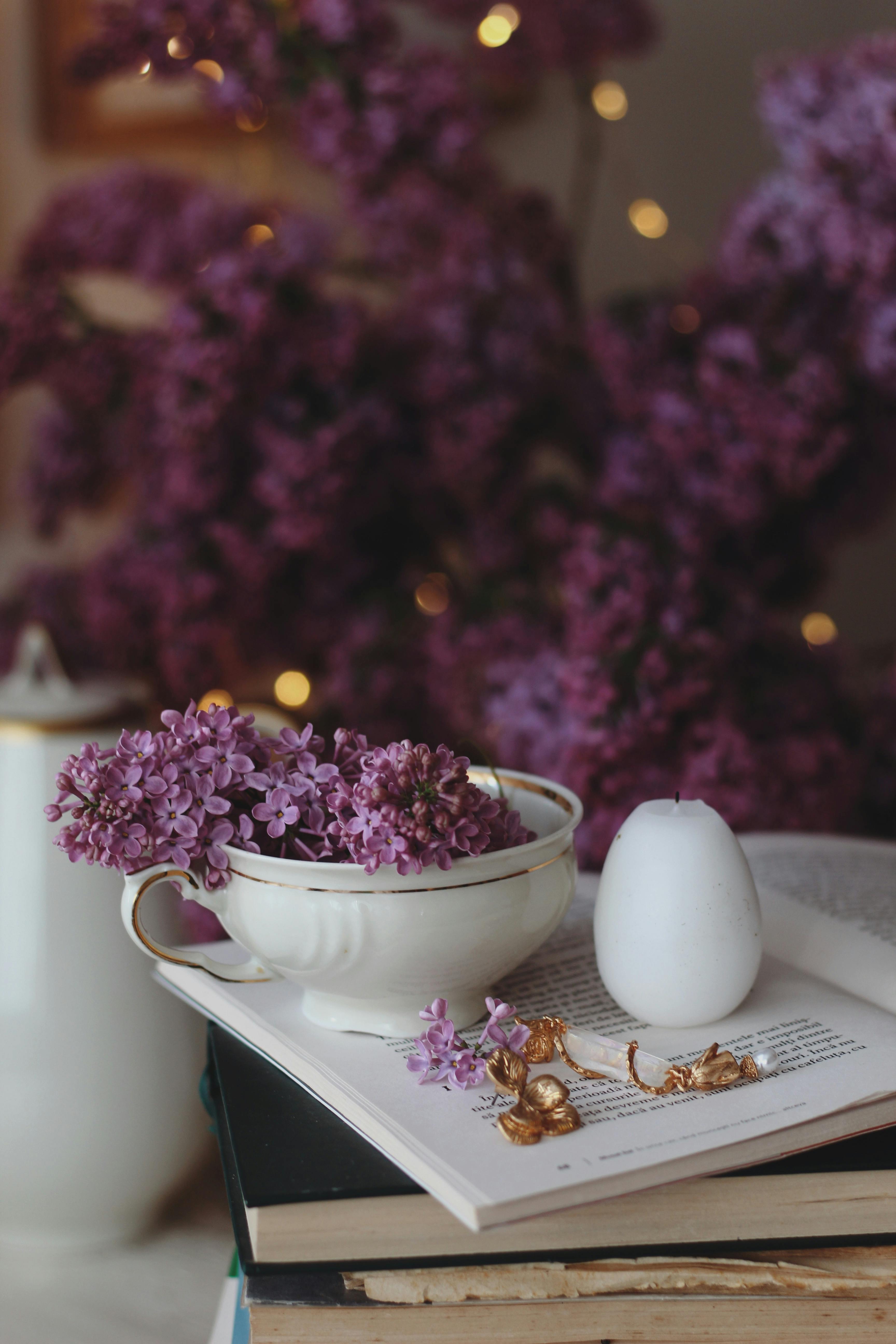 A serene scene featuring lilacs in a cup next to a candle and open book. Perfect for relaxation themes.