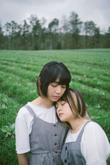 Two young women embracing tenderly in a lush green field, exuding peace and closeness.