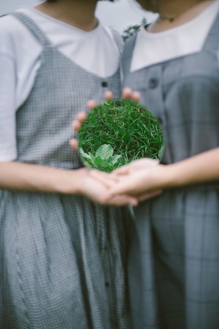 Two women holding a mirror with a reflection of green grass.