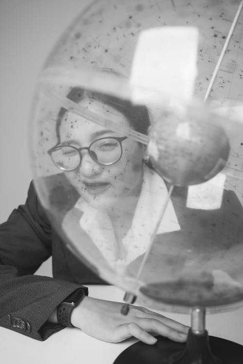 A Grayscale of a Woman Looking at a Transparent Globe