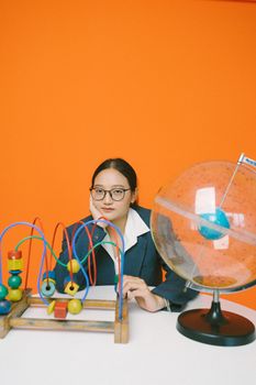 Asian woman in suit with educational toys and globe on orange background. Studio shot with copy space.