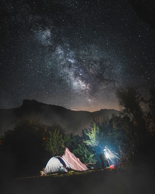 Free A serene camping scene under a starry sky with visible Milky Way in a mountainous area. Stock Photo