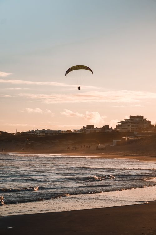 Free Paraglider soaring above a tranquil beach during sunset, capturing summer's essence. Stock Photo