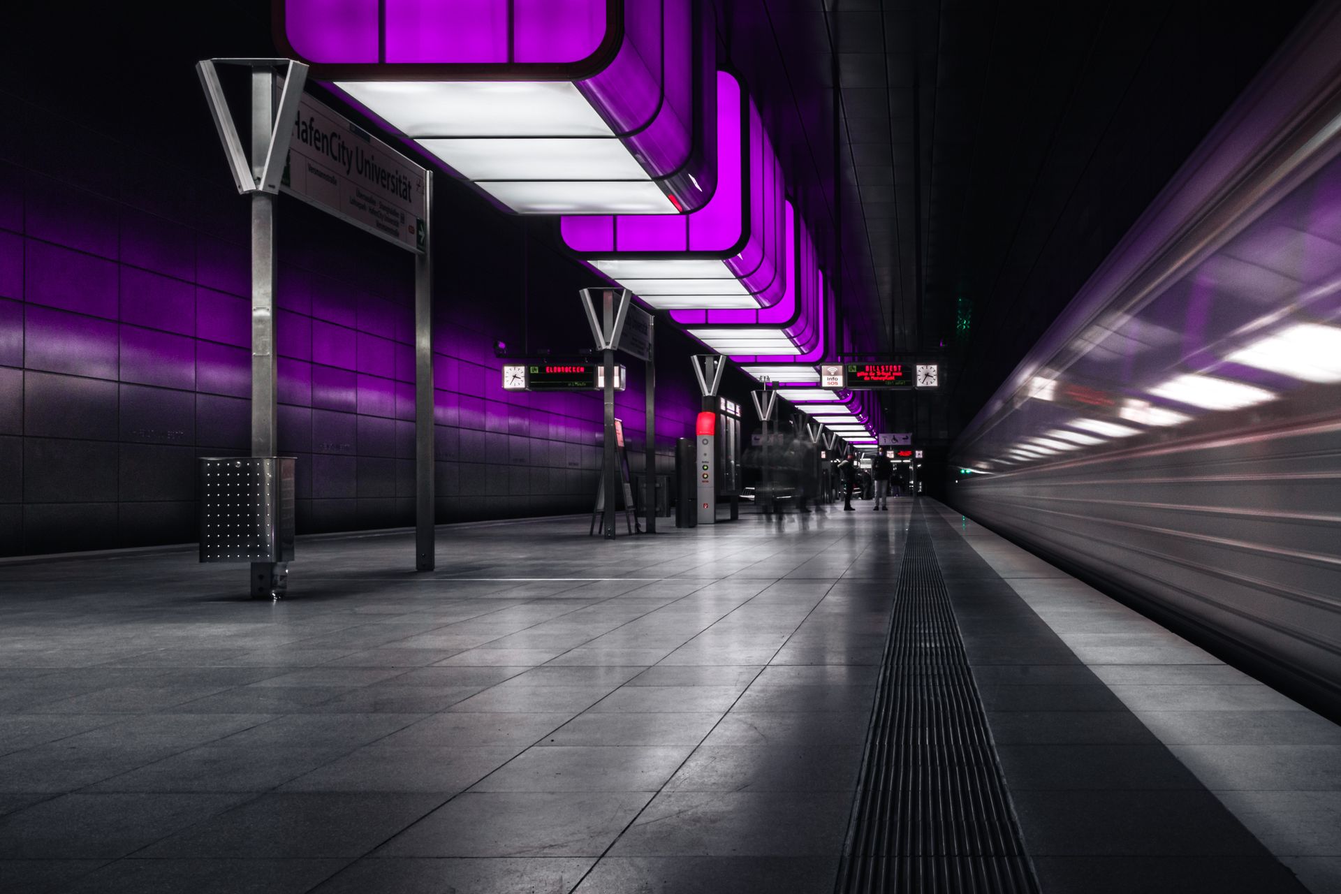 Purple-lit subway station with motion blur of passing train at HafenCity Universität in Hamburg.