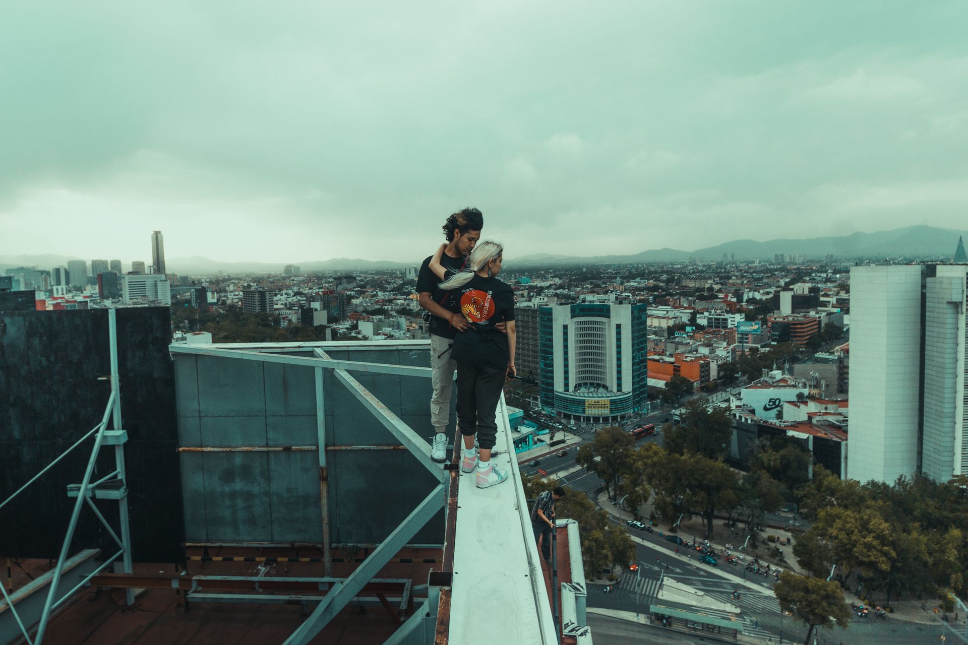 Young couple standing on skyscraper edge in urban Mexico City, showcasing adventure and modern city life.