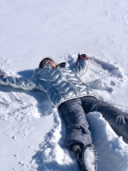 Woman in winter clothing making a snow angel on a bright winter day.