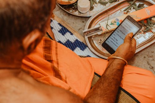 Free A person in traditional attire reads a script on a smartphone during a cultural ceremony. Stock Photo
