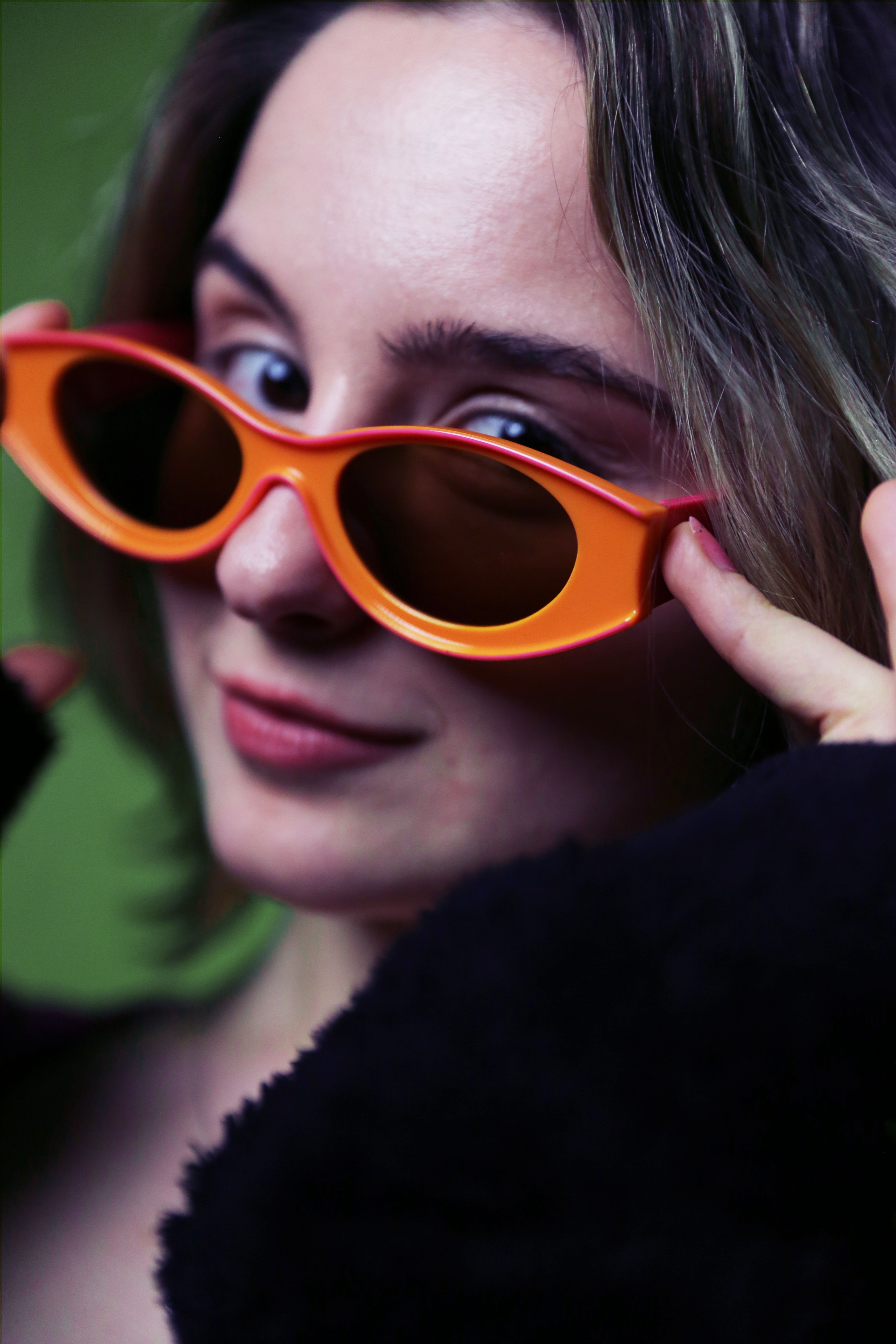 Close-up portrait of a stylish young woman wearing funky orange sunglasses, adding a playful twist to her look.