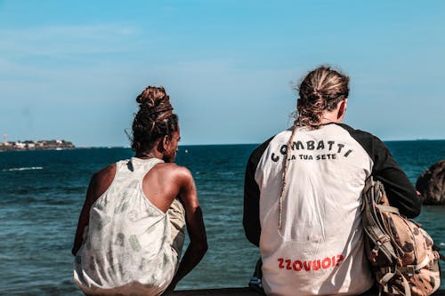 Two Man Sitting on Seawall in Front of Seashore