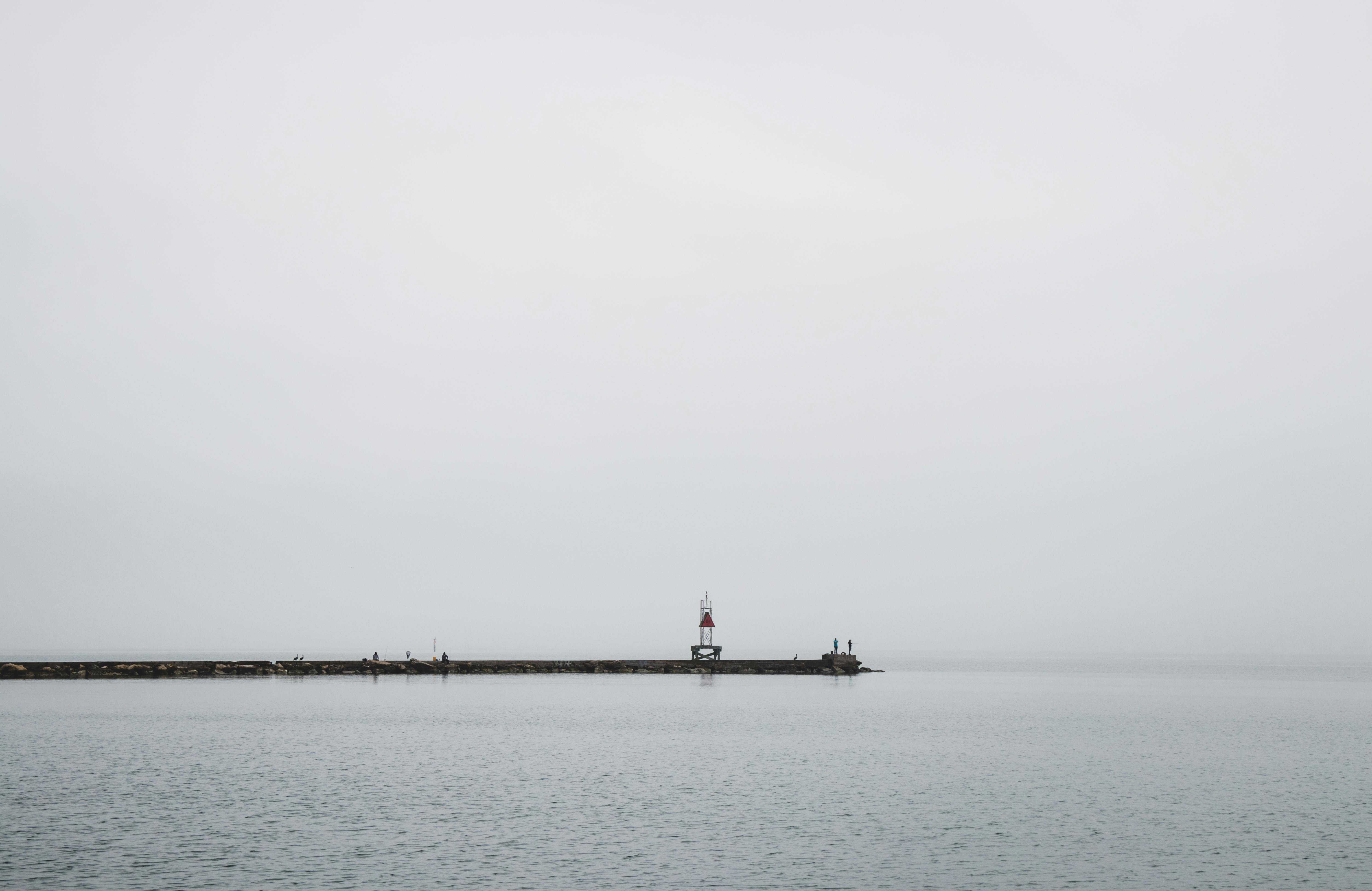 码头的灯塔在灰色天空下延伸，融入薄雾笼罩的宁静海面
