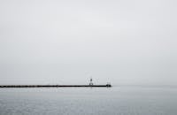 码头的灯塔在灰色天空下延伸，融入薄雾笼罩的宁静海面