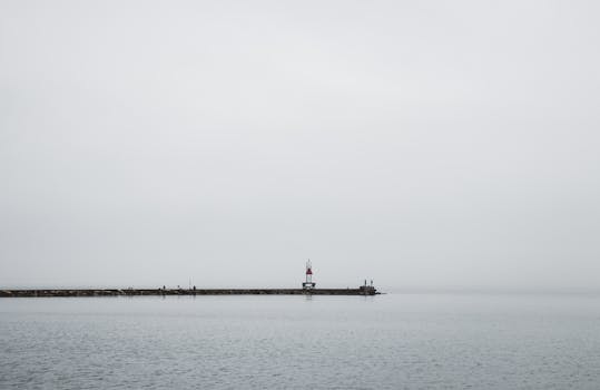 码头的灯塔在灰色天空下延伸，融入薄雾笼罩的宁静海面